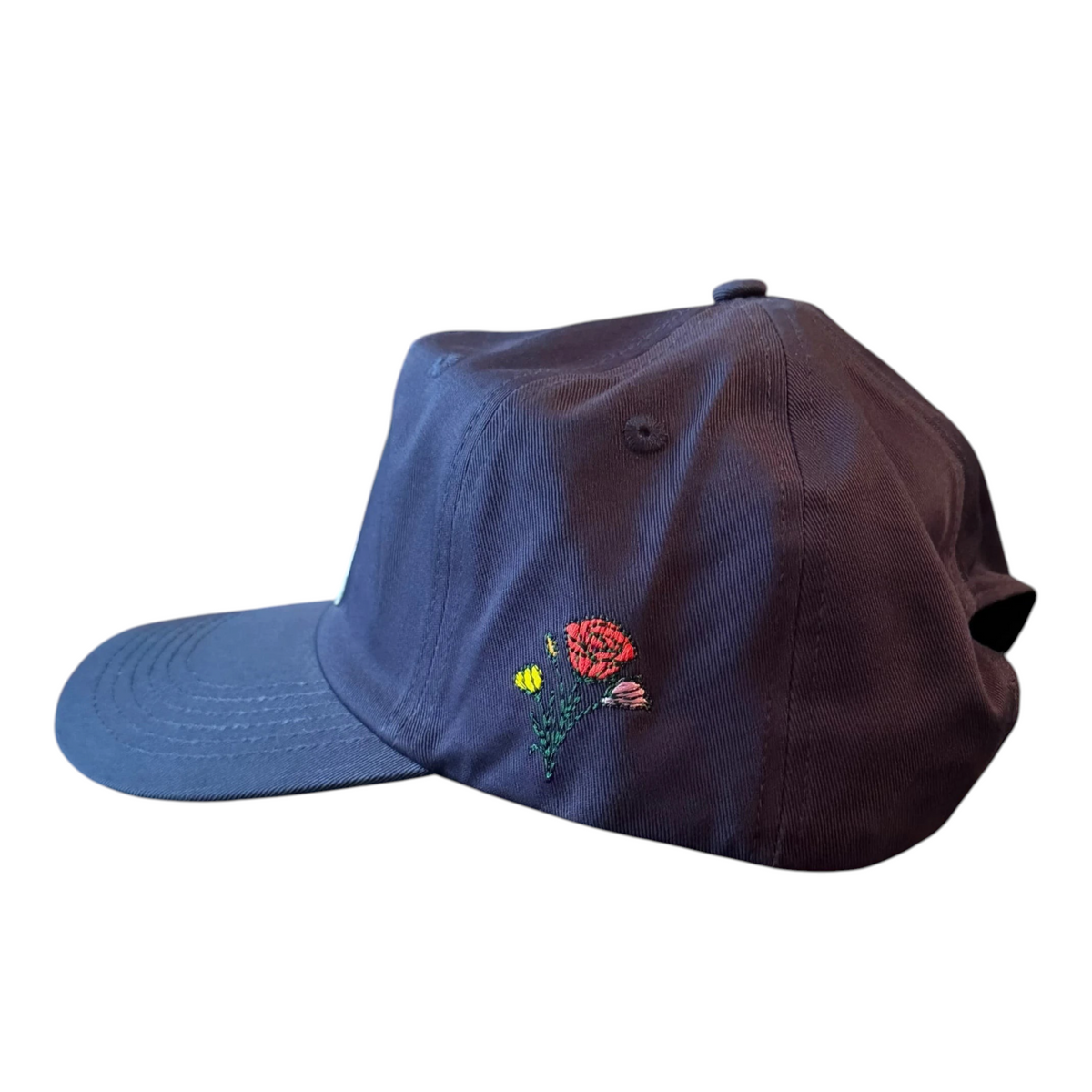 AMPLE navy blue cotton twill baseball cap with side embroidery featuring a red floral motif on a glass table